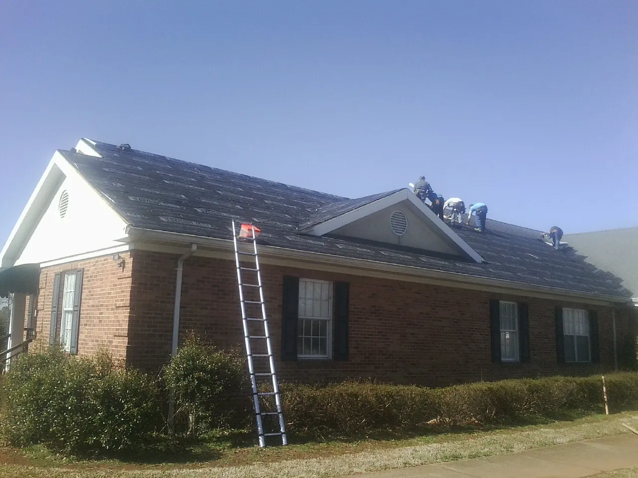 Crew tearing shingles off a brick ranch roof with a ladder set — Emergency Roof Repair work by our crew in Bear Lake