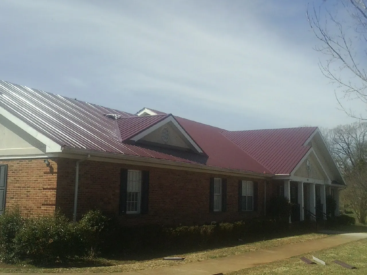 Red metal roof with gabled entries on a long brick building, from a Hail Damage Roof Repair job in Bear Lake