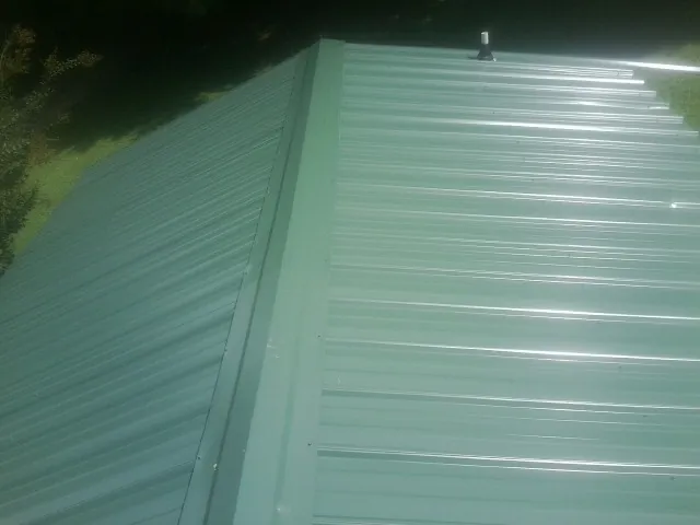 New green metal panels meeting at the ridge of a roof — Flat Roof Repair work by our crew in Bear Lake