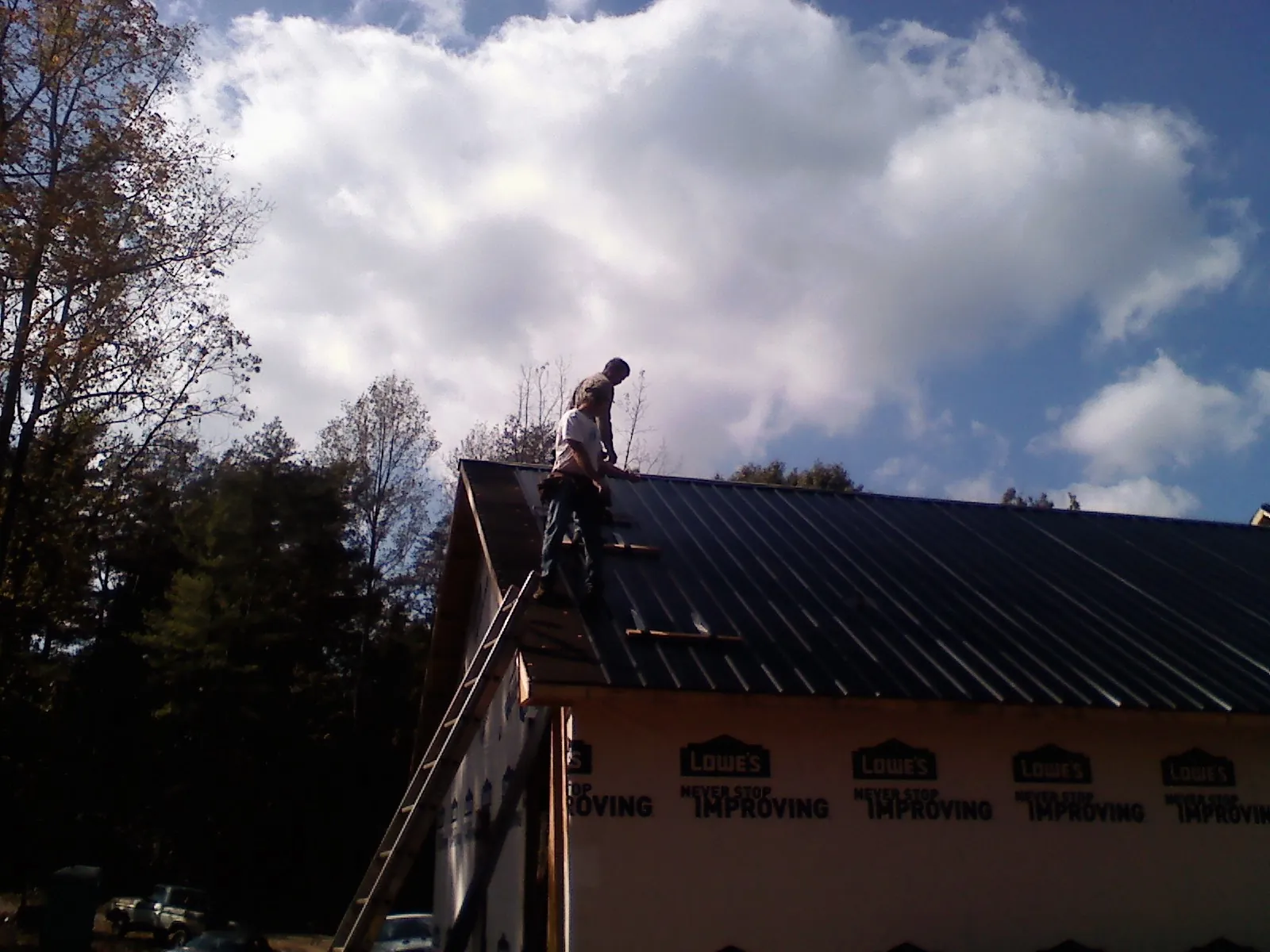 Roofer fastening dark metal panels high against a cloudy sky, from a Roof Inspection job in Bear Lake