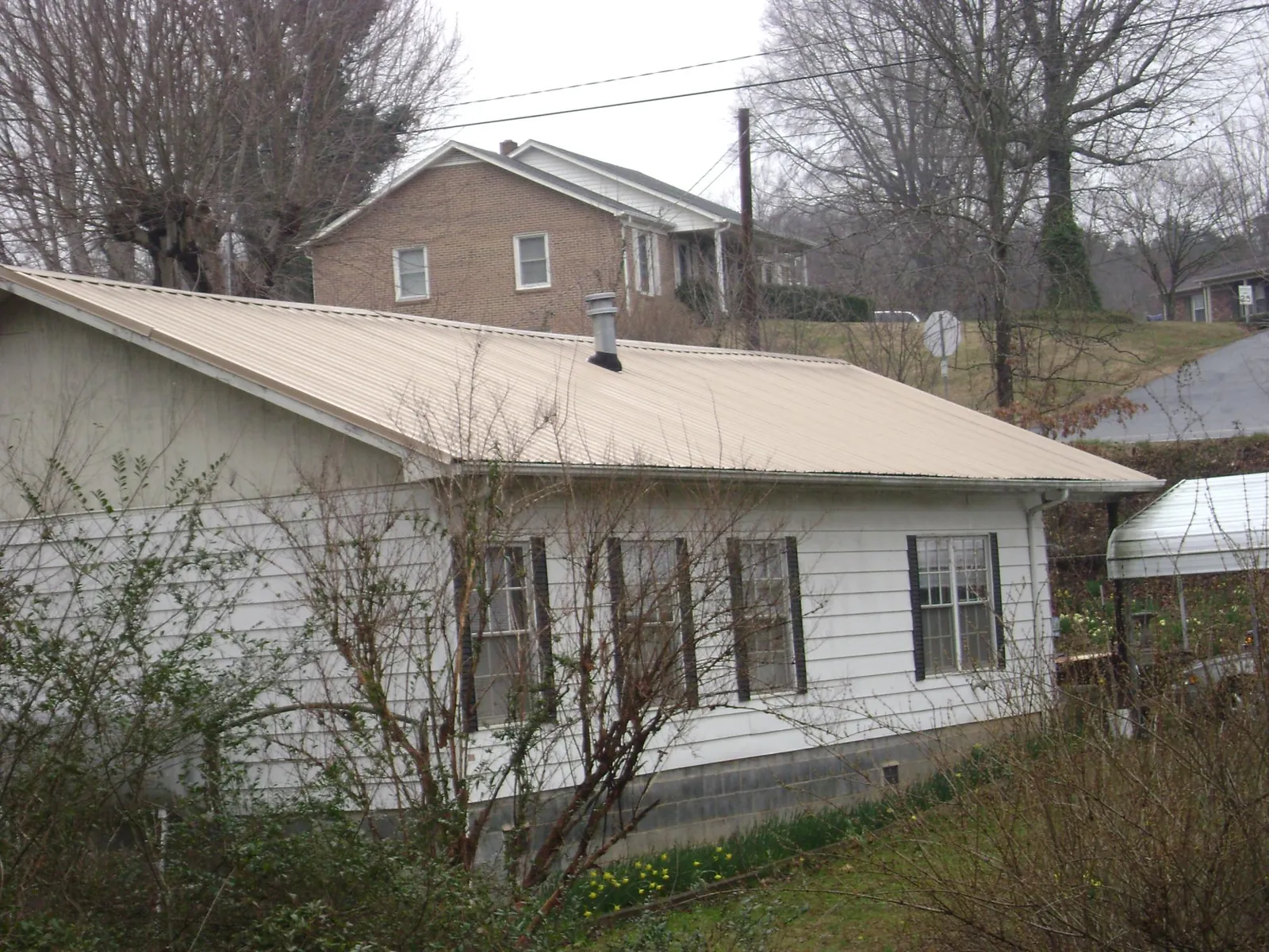 Tan metal roof on a white sided house set into a hillside — Commercial Roofing by Roofing Brothers in Bear Lake
