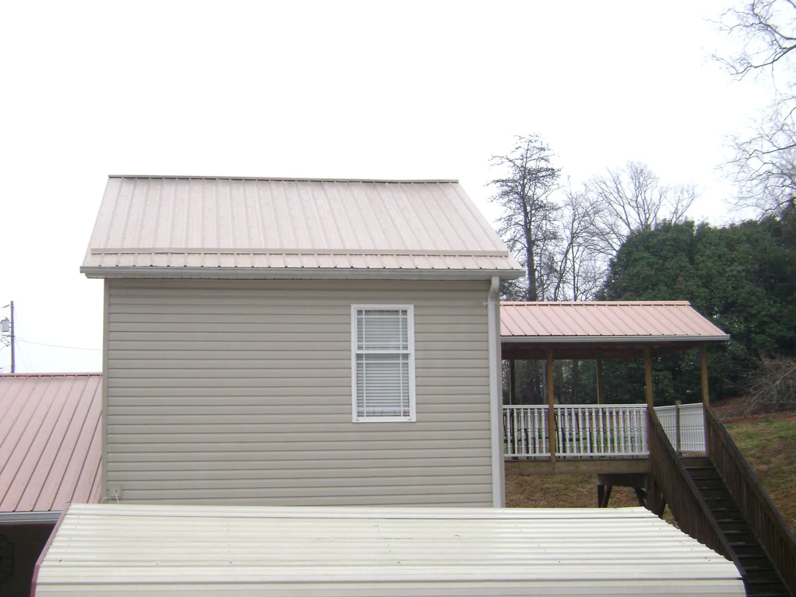 Tan metal roofs on a two story addition and attached porch, from a Roof Replacement job in Bear Lake